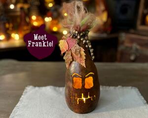 A spooky monster gourd decoration with a battery-operated candle. His name is Frankie and is adorned with crazy hair, leaves, and berries.